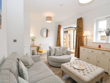 A living room with a gray sofa a round chair an ottoman and a sideboard with lamps and curtains at The Hollies in Norwich