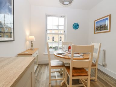 A dining room with a round wooden table set for four and a window showing exterior buildings at The Hollies in Norwich