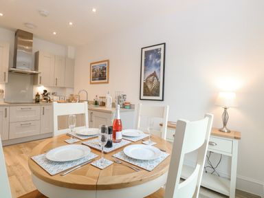 A kitchen with a round dining table set for four with plates glasses and a bottle at The Hollies in Norwich