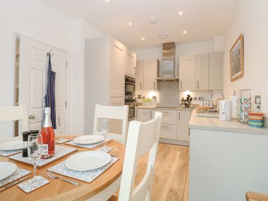 A kitchen and dining area with a wooden table set with plates and glasses and white chairs at The Hollies in Norwich