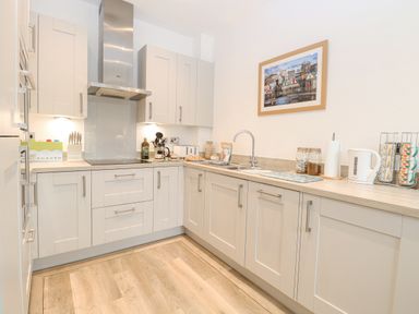 A kitchen with white cabinets a stove a sink a kettle and a framed picture on the wall at The Hollies in Norwich