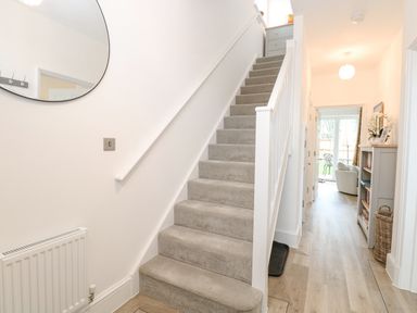 A hallway with carpeted stairs and wooden floor leading to a living area at The Hollies in Norwich