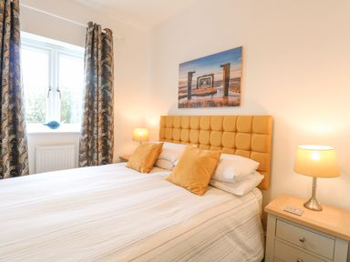 A bedroom with a bed with orange headboard and pillows bedside tables with lamps and a window with patterned curtains at The Hollies in Norwich