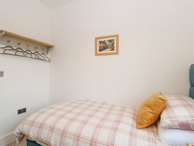 A bedroom with a single bed a checkered duvet a yellow pillow hangers on a wall shelf and a framed picture at The Hollies in Norwich