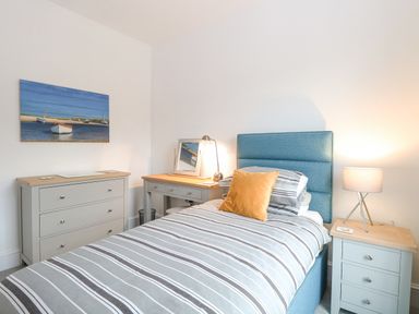 A bedroom with a single bed with striped bedding and yellow pillow next to a bedside table with lamp and a chest of drawers with a painting on the wall at The Hollies in Norwich