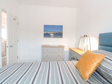 A bedroom with striped bedding a yellow pillow a dresser a desk with a mirror and a lamp and a painting of boats on the wall at The Hollies in Norwich
