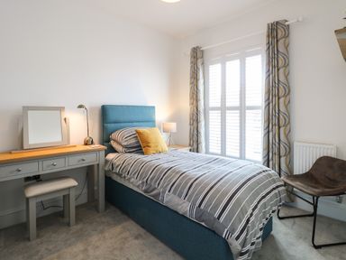 A bedroom with a single bed a striped duvet a dressing table with a mirror and lamp and a chair at The Hollies in Norwich