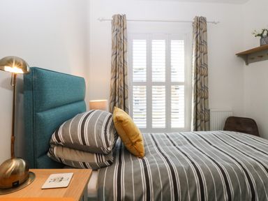A bedroom with striped bedding a blue headboard and patterned curtains at The Hollies in Norwich
