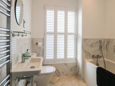 A bathroom with a sink toilet bathtub window with shutters and a towel at The Hollies in Norwich
