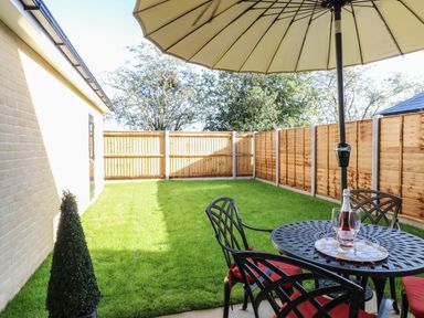 A backyard with a lawn umbrella table and chairs on a patio at The Hollies in Norwich