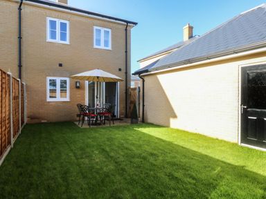 A backyard with a patio table and umbrella set on grass next to a brick house and a building at The Hollies in Norwich