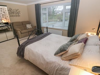 A bedroom with a double bed pillows and blanket a window with blinds a sofa a wall mirror and curtains at Garden View in Pembroke