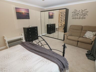 A bedroom with a bed dressed with a white comforter and gray throw a black chest of drawers mirrored wardrobe a beige loveseat with a decorative pillow and wall art at Garden View in Pembroke