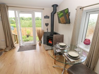 A dining area with a round glass table set for two next to a wood burning stove and double glass doors in Garden View Pembroke