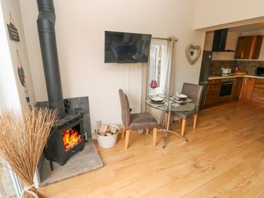 A kitchen and dining area with a wood burning stove a glass table with two chairs and a wall mounted television at Garden View in Pembroke