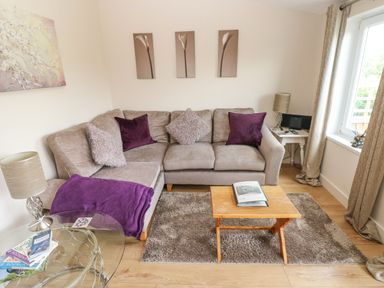 A living room with a beige sectional sofa purple and beige cushions a wooden coffee table and paintings on the wall at Garden View in Pembroke