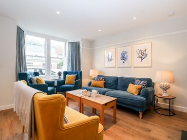A living room with blue and yellow chairs a wooden coffee table and framed artwork on the wall at Fawcett Cottage in Aldeburgh