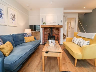 A living room with blue and yellow sofas a wooden coffee table and a fireplace at Fawcett Cottage in Aldeburgh