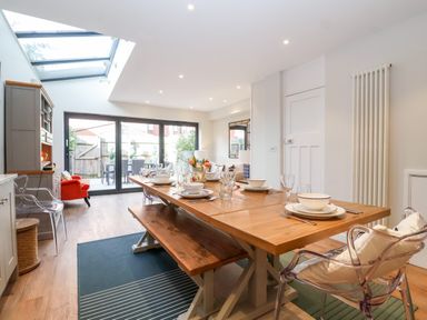 A dining area with a wooden table set for meals and glass doors leading to an outdoor patio at Fawcett Cottage in Aldeburgh