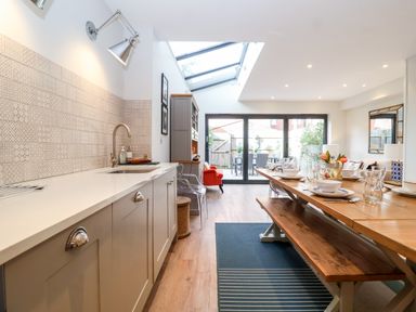 A kitchen and dining area with a long wooden table set for a meal and glass doors leading to a garden at Fawcett Cottage in Aldeburgh