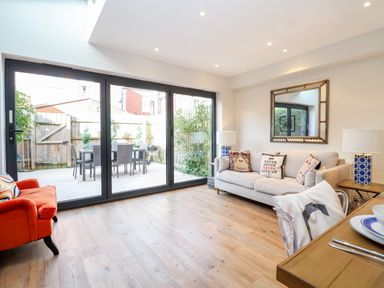 A living room with large glass doors opening to a patio with table and chairs at Fawcett Cottage in Aldeburgh
