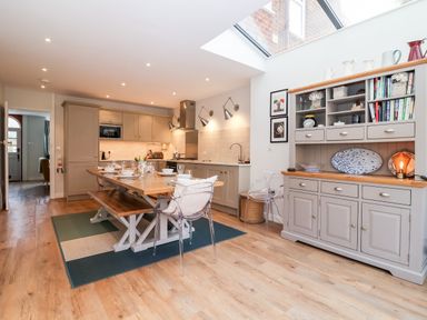 A kitchen with a wooden dining table and bench a gray cabinet with shelves and a skylight at Fawcett Cottage in Aldeburgh