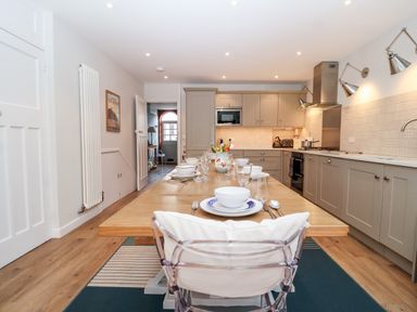 A kitchen with a long dining table set with plates glasses and cutlery at Fawcett Cottage in Aldeburgh