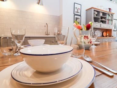 A dining table set with plates bowls glasses and cutlery with a jug of flowers in a kitchen at Fawcett Cottage in Aldeburgh