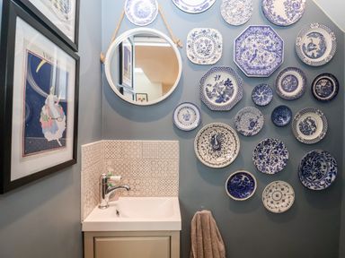 A small bathroom sink with patterned tiles a round mirror and blue and white decorative plates on a wall at Fawcett Cottage in Aldeburgh