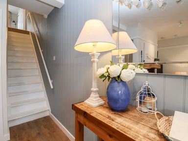 A staircase next to a wooden table with a lamp a blue vase with white flowers and a candle holder at Fawcett Cottage in Aldeburgh