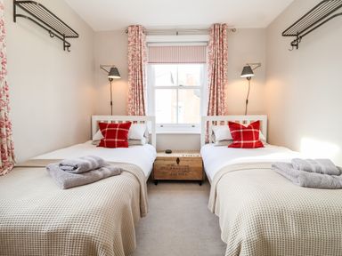 A bedroom with two single beds with red pillows and towels on beige blankets at Fawcett Cottage in Aldeburgh