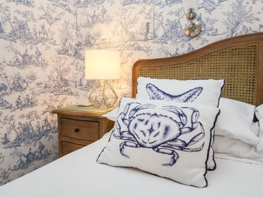 A bedroom with pillows featuring crab and starfish designs on a bed with a wooden headboard and a bedside table with a lamp at Fawcett Cottage in Aldeburgh