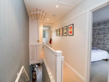 A hallway with framed pictures on the wall next to a bedroom with patterned wallpaper at Fawcett Cottage in Aldeburgh