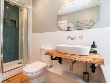 A bathroom with a wooden countertop sink a toilet a shower with green tiles and a wall mirror at Fawcett Cottage in Aldeburgh