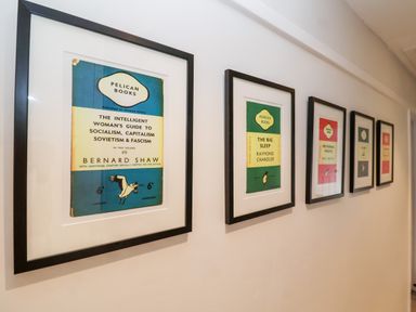 A hallway with framed vintage book cover prints hung on a white wall at Fawcett Cottage in Aldeburgh