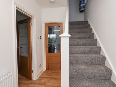 A hallway with wooden doors and a carpeted staircase at Maywood in Seahouses