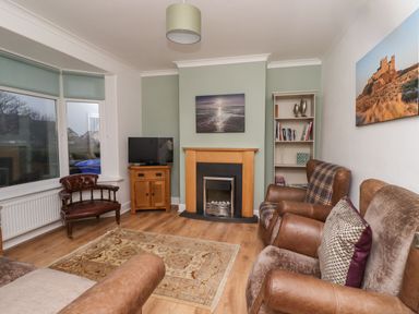 A living room with leather chairs a wooden cabinet a fireplace and a bookshelf at Maywood in Seahouses