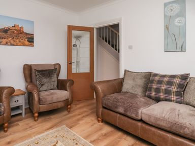 A living room with a sofa and armchairs with cushions a wooden floor and paintings on the walls at Maywood in Seahouses