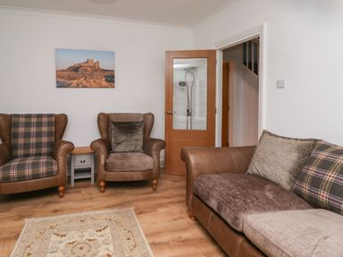 A sitting area with two armchairs and a sofa a wooden side table and a door with glass panel at Maywood in Seahouses