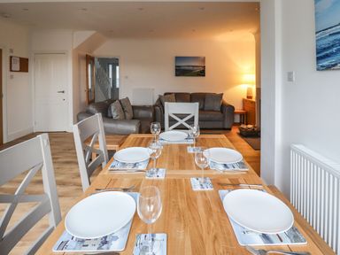 A dining table set with plates and glasses in front of a living room with sofas at Maywood in Seahouses