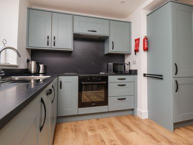A kitchen with blue cabinets black countertop oven microwave and wooden floor at Maywood in Seahouses