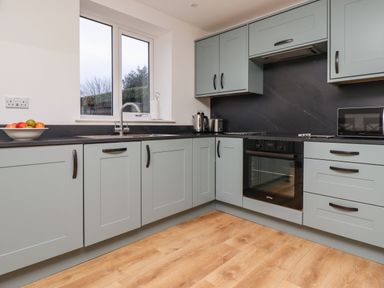A kitchen with light blue cabinets a black countertop a sink under a window and built in oven at Maywood in Seahouses