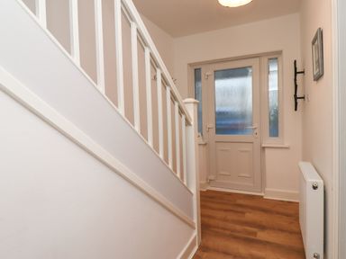 A hallway with a white staircase and a door with frosted glass at Maywood in Seahouses