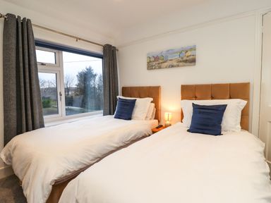 A bedroom with two single beds white bedding blue pillows a window with curtains and a painting on the wall at Maywood in Seahouses