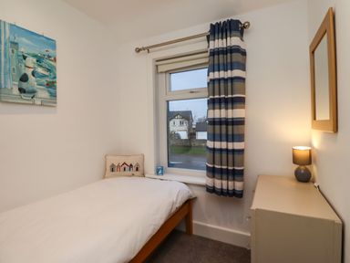 A small bedroom with a bed a window with striped curtains a painting a mirror a lamp and a cushion at Maywood in Seahouses