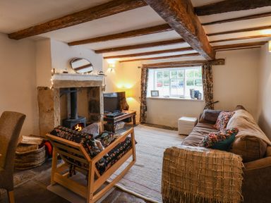 A living room with exposed wooden beams a fireplace a sofa and a wooden armchair at Lythe Cottage in Lythe