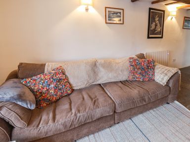 A brown sofa with colorful cushions and a beige throw blanket in a living room at Lythe Cottage in Lythe