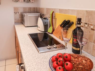 A kitchen counter with a microwave toaster stovetop knives wine bottle and glasses tomatoes and bread at Lythe Cottage in Lythe
