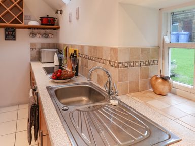 A kitchen sink with a faucet next to a countertop with bread tomatoes wine glasses and a microwave at Lythe Cottage in Lythe