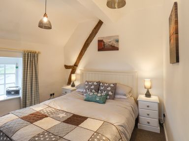 A bedroom with a double bed two bedside tables with lamps a window with checkered curtains and wooden beam at Lythe Cottage in Lythe